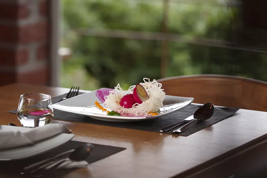 Un plato servido con flores comestibles sobre una mesa oscura, junto a una ventana hacia el jardín