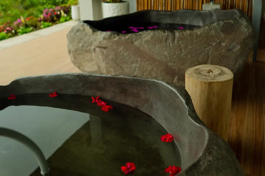 Dos tinas talladas en piedra volcánica, con agua y pétalos rojos, en la terraza del lodge