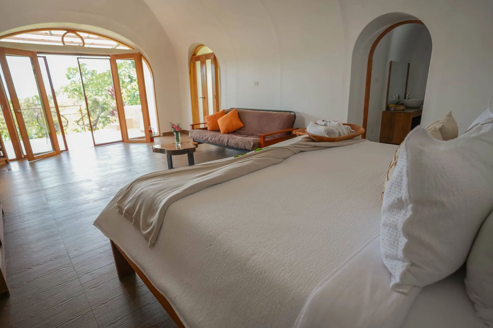 A dome seen from the head of the bed: a sofa with orange cushions, a small table and an arched doorway at the back