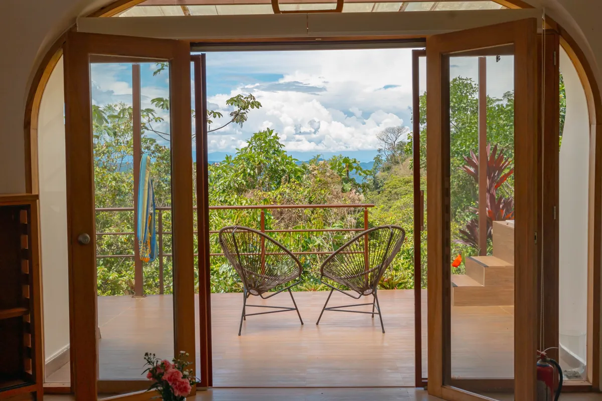 Puertas de habitación que se abren a una terraza de madera con dos sillas sobre el valle